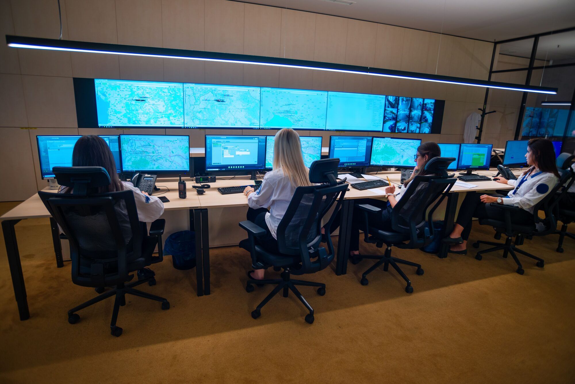 A team monitoring network maps and system dashboards across a wall of screens in an operations center